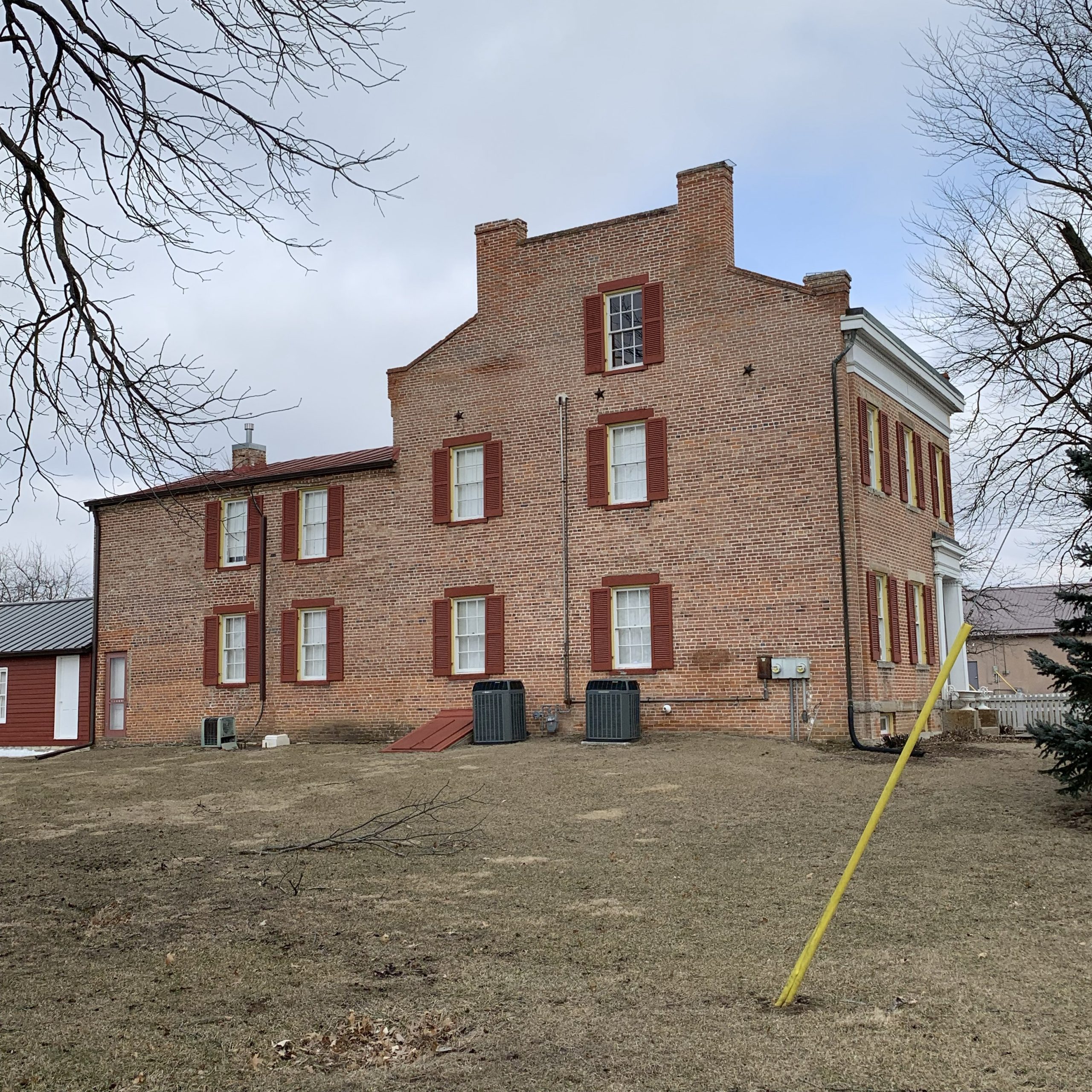 Brick building with red shutters on a wintery, leafless-tree street and an empty dirt lot in front.